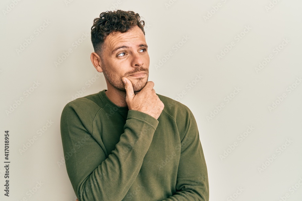 Young hispanic man wearing casual clothes with hand on chin thinking about question, pensive expression. smiling with thoughtful face. doubt concept. Young hispanic man wearing casual clothes with hand on chin thinking about question, pensive expression. smiling with thoughtful face. doubt concept.