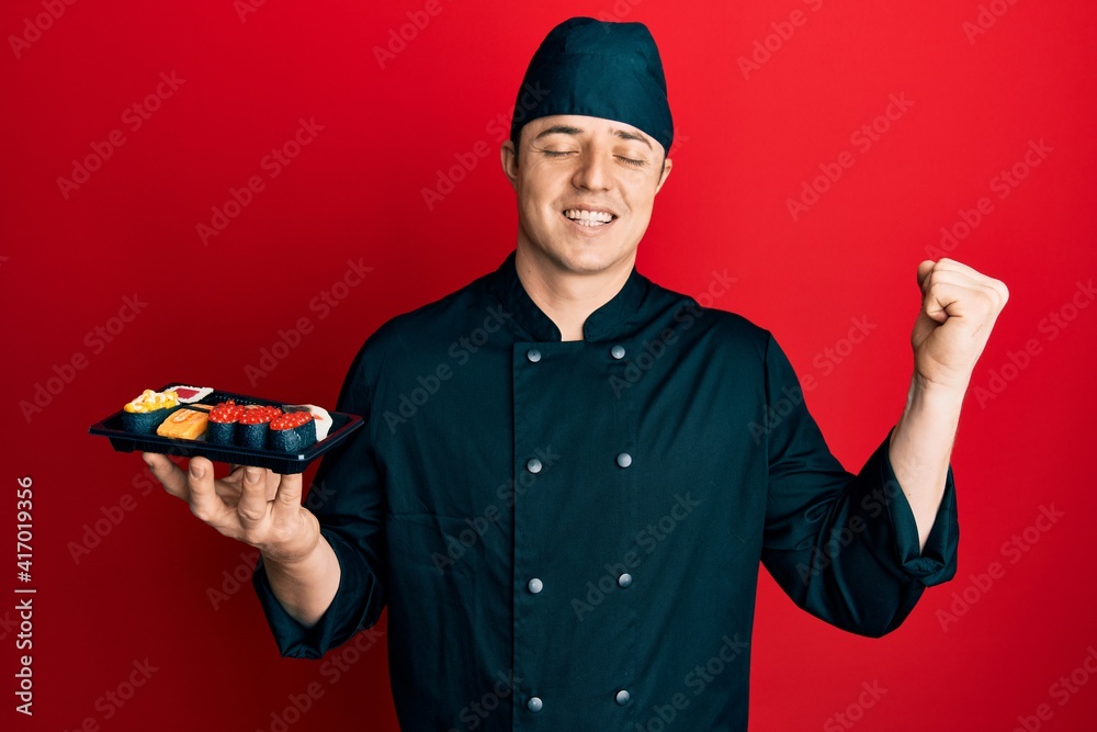 Handsome young man wearing chef uniform holding plate of sushi screaming proud, celebrating victory and success very excited with raised arm Handsome young man wearing chef uniform holding plate of sushi screaming proud, celebrating victory and success very excited with raised arm