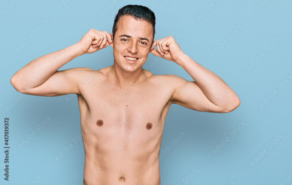 Handsome young man wearing swimwear shirtless smiling pulling ears with fingers, funny gesture. audition problem