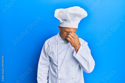 Middle age grey-haired man wearing professional cook uniform and hat tired rubbing nose and eyes feeling fatigue and headache. stress and frustration concept.