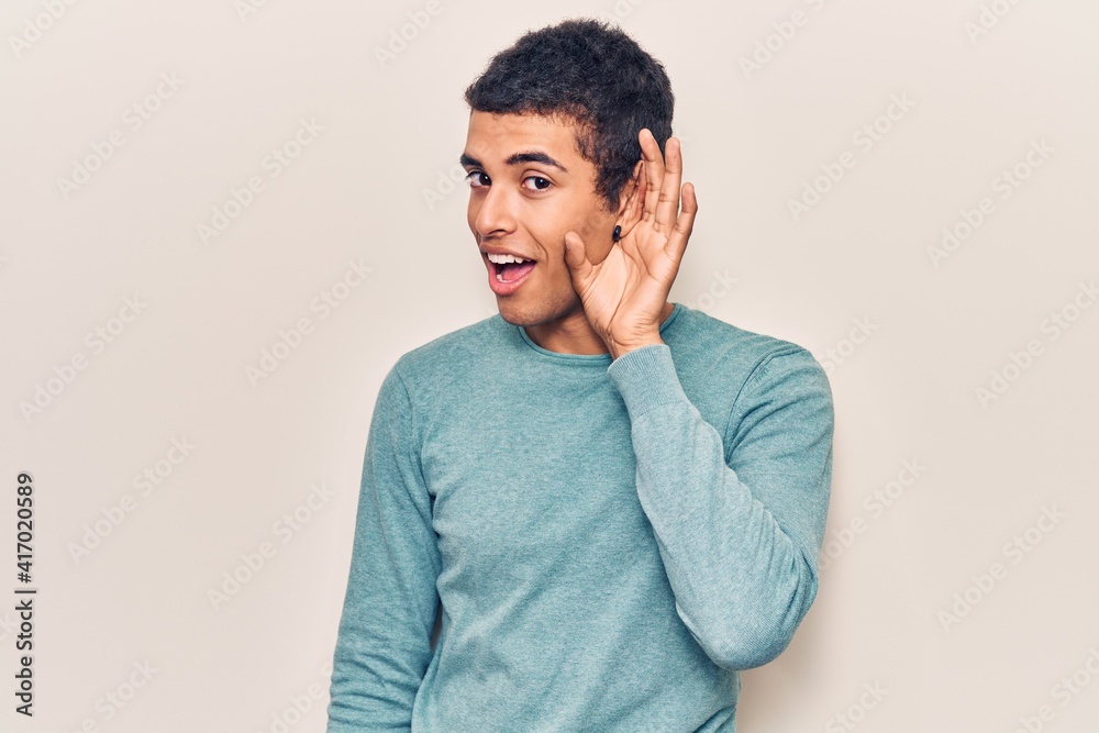 Young african amercian man wearing casual clothes smiling with hand over ear listening and hearing to rumor or gossip. deafness concept. Young african amercian man wearing casual clothes smiling with hand over ear listening and hearing to rumor or gossip. deafness concept.