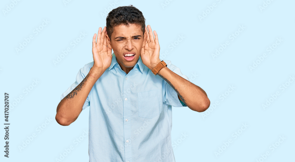 Young handsome african american man wearing casual clothes trying to hear both hands on ear gesture, curious for gossip. hearing problem, deaf Young handsome african american man wearing casual clothes trying to hear both hands on ear gesture, curious for gossip. hearing problem, deaf