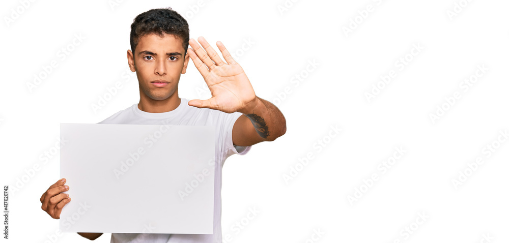 Young handsome african american man holding blank empty banner with open hand doing stop sign with serious and confident expression, defense gesture Young handsome african american man holding blank empty banner with open hand doing stop sign with serious and confident expression, defense gesture