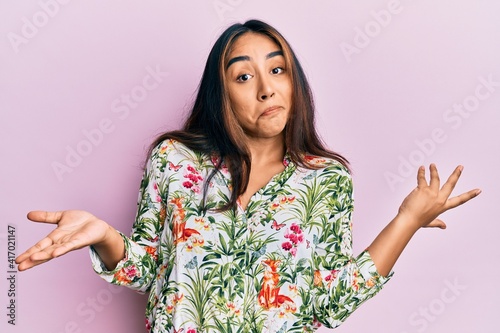 Young latin woman wearing casual clothes clueless and confused expression with arms and hands raised. doubt concept.