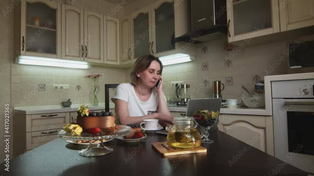 Woman drinks coffee, eats cake and talks on phone at kitchen Woman drinks coffee, eats cake and talks on phone at kitchen