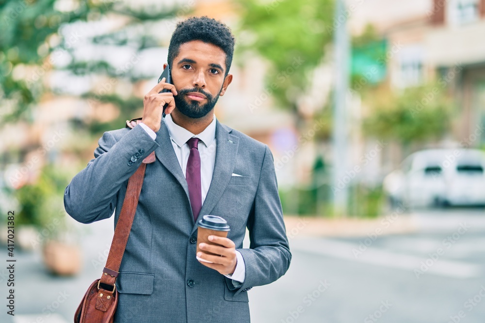Young african american businessman with serious expression talking on the smartphone and drinking coffee at the city. Young african american businessman with serious expression talking on the smartphone and drinking coffee at the city.