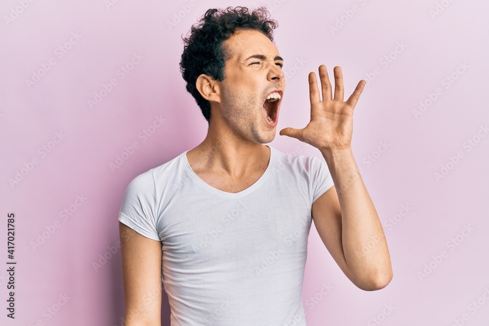 Young handsome man wearing casual white t shirt shouting and screaming loud to side with hand on mouth. communication concept. Young handsome man wearing casual white t shirt shouting and screaming loud to side with hand on mouth. communication concept.