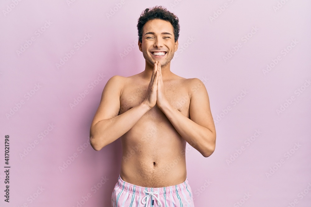 Fototapeta premium Young handsome man wearing swimwear shirtless praying with hands together asking for forgiveness smiling confident.