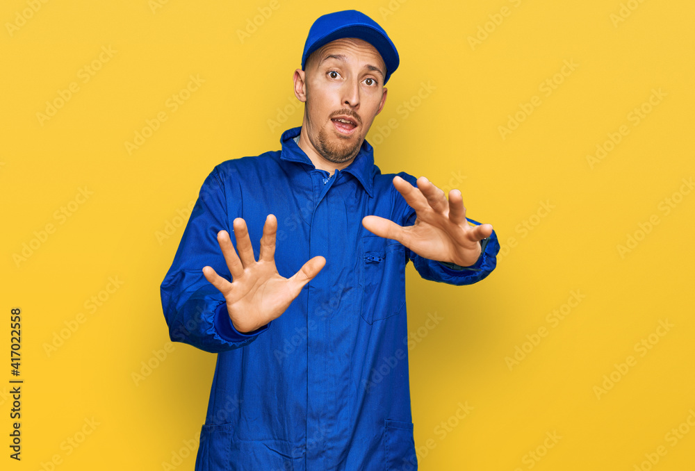 Bald man with beard wearing builder jumpsuit uniform afraid and terrified with fear expression stop gesture with hands, shouting in shock. panic concept. Bald man with beard wearing builder jumpsuit uniform afraid and terrified with fear expression stop gesture with hands, shouting in shock. panic concept.