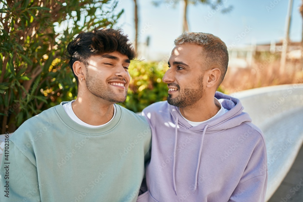 Young gay couple smiling happy sitting on the bench at the city.