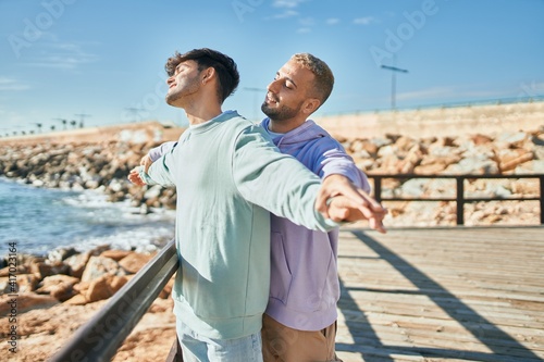 Young gay couple breathing with arms opened at the beach.