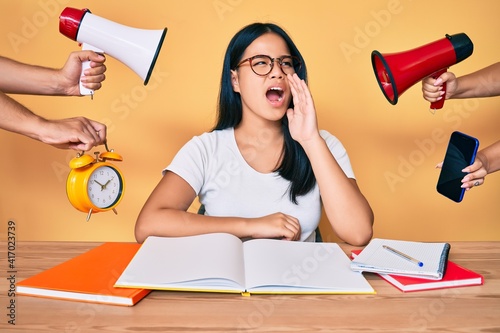 Young beautiful asian girl stuying for university getting stressed out shouting and screaming loud to side with hand on mouth. communication concept.