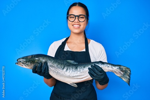 Young beautiful asian girl fishmonger selling fresh raw salmon smiling with a happy and cool smile on face. showing teeth.