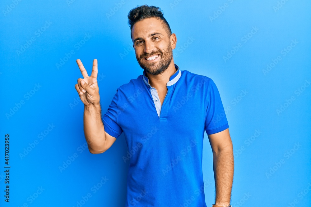 Handsome man with beard wearing casual clothes smiling with happy face winking at the camera doing victory sign. number two. Handsome man with beard wearing casual clothes smiling with happy face winking at the camera doing victory sign. number two.