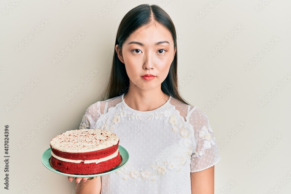 Young chinese woman holding carrot cake thinking attitude and sober expression looking self confident Young chinese woman holding carrot cake thinking attitude and sober expression looking self confident