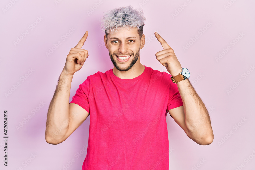 Young hispanic man with modern dyed hair wearing casual pink t shirt smiling pointing to head with both hands finger, great idea or thought, good memory
