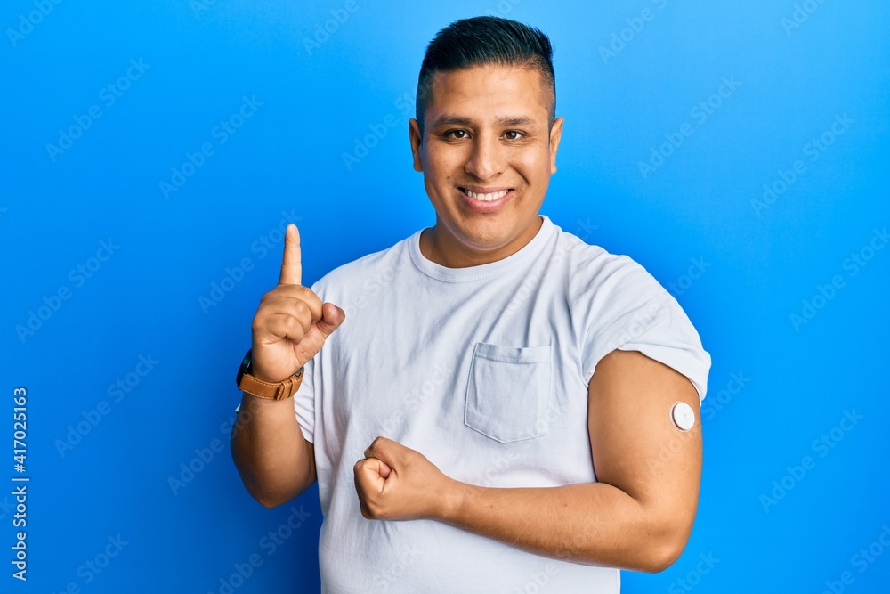 Young latin man using glucose meter button smiling with an idea or question pointing finger with happy face, number one Young latin man using glucose meter button smiling with an idea or question pointing finger with happy face, number one