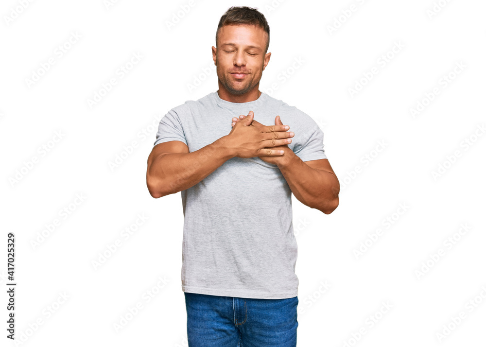 Handsome muscle man wearing casual grey tshirt smiling with hands on chest with closed eyes and grateful gesture on face. health concept. Handsome muscle man wearing casual grey tshirt smiling with hands on chest with closed eyes and grateful gesture on face. health concept.