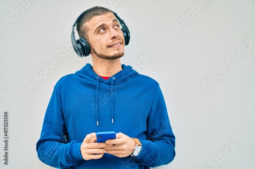 Young hispanic man smiling happy using smartphone and headphones at the city. © Krakenimages.com