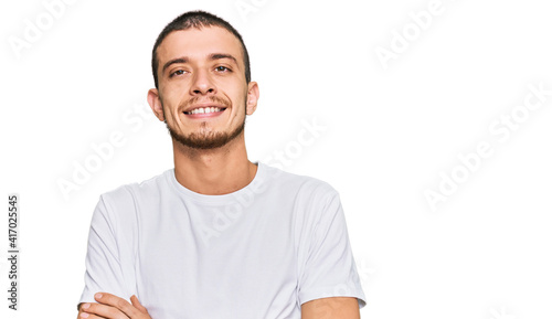 Hispanic young man wearing casual white t shirt happy face smiling with crossed arms looking at the camera. positive person. © Krakenimages.com
