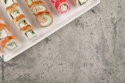 A white board with different types of delicious sushi rolls on stone table