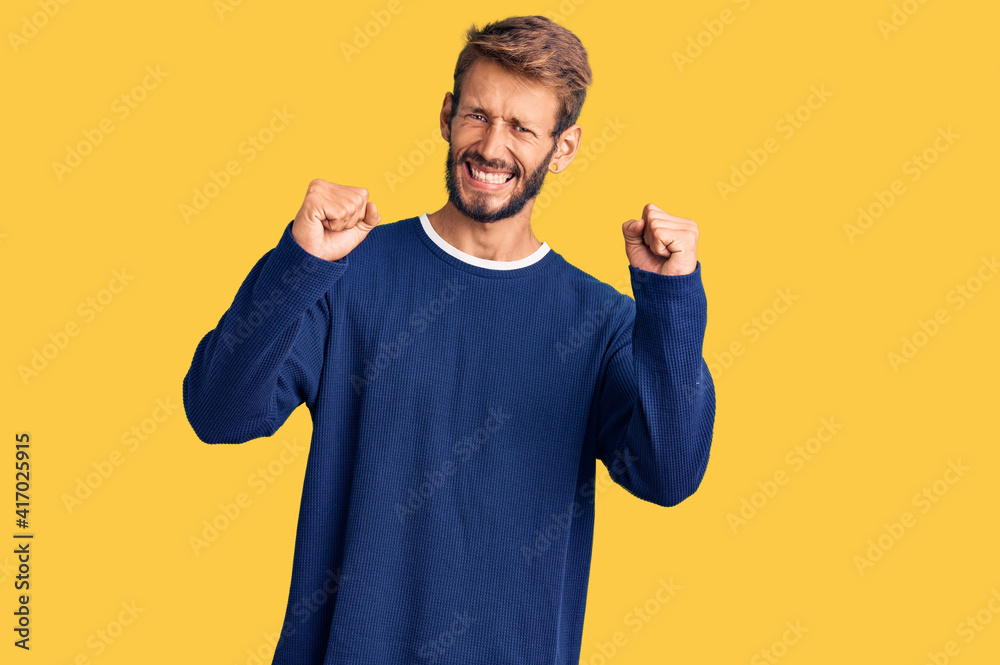Handsome blond man with beard wearing casual sweater angry and mad raising fists frustrated and furious while shouting with anger. rage and aggressive concept. Handsome blond man with beard wearing casual sweater angry and mad raising fists frustrated and furious while shouting with anger. rage and aggressive concept.