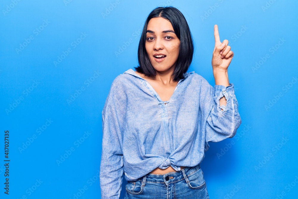 Young beautiful latin woman wearing casual clothes pointing finger up with successful idea. exited and happy. number one. Young beautiful latin woman wearing casual clothes pointing finger up with successful idea. exited and happy. number one.