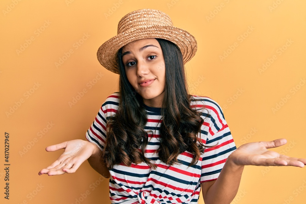 Young hispanic woman wearing summer hat clueless and confused expression with arms and hands raised. doubt concept. Young hispanic woman wearing summer hat clueless and confused expression with arms and hands raised. doubt concept.