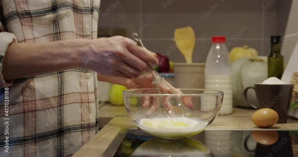 Human hands mixing egg and milk with a whisk in a bowl in kitchen indoors. Human hands mixing egg and milk with a whisk in a bowl in kitchen indoors.