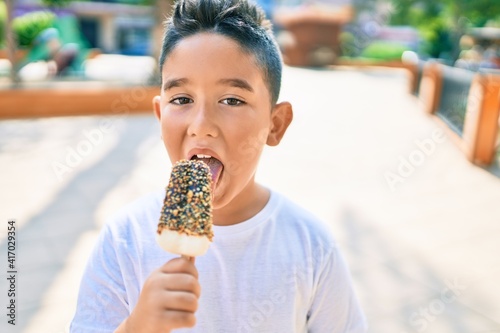 Adorable boy smiling happy eating ice cream standing at street of city.