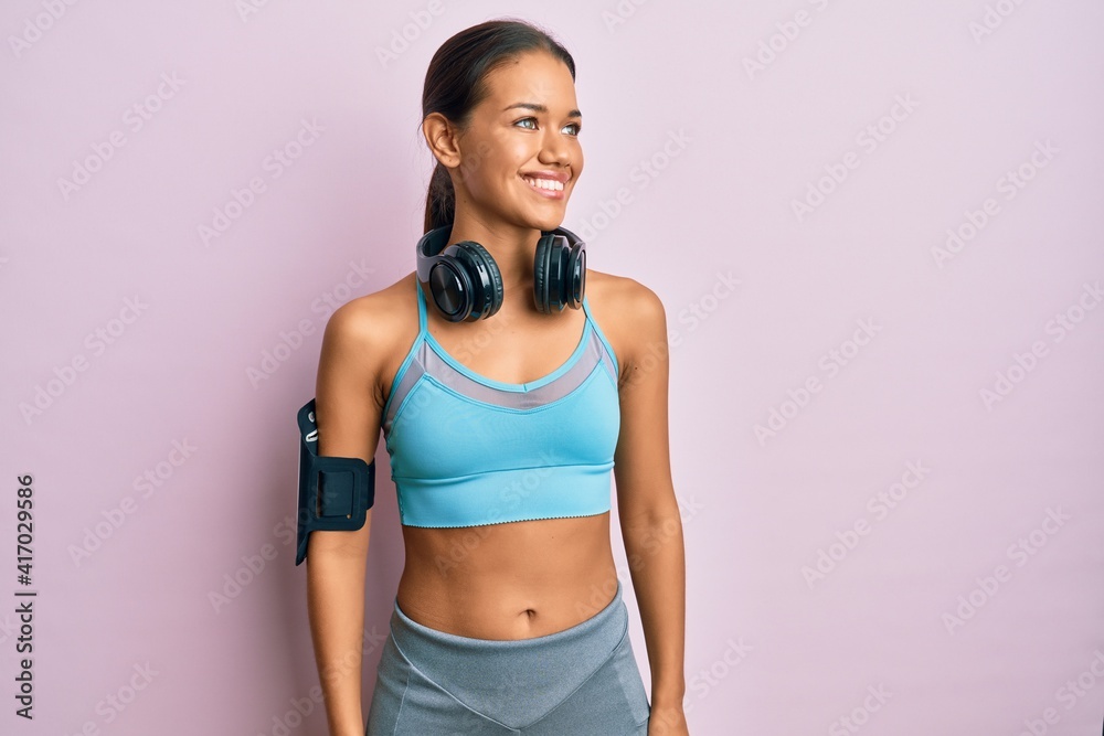 Beautiful hispanic woman wearing sportswear and headphones looking to side, relax profile pose with natural face and confident smile.