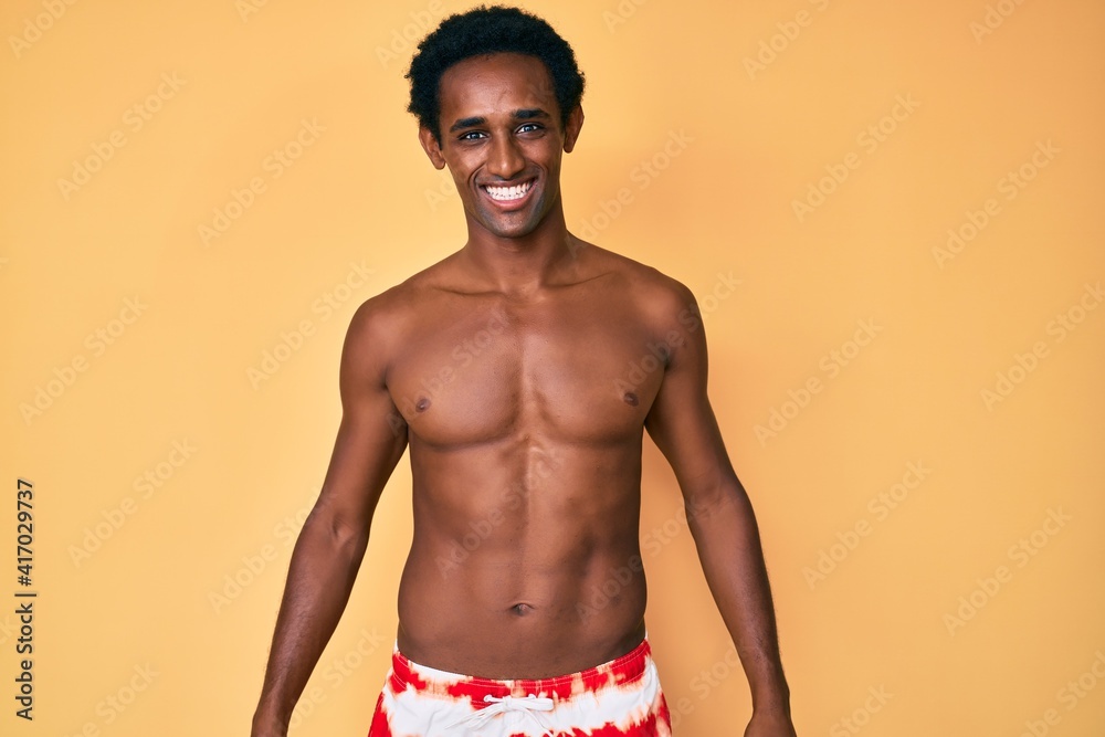 African handsome man wearing swimsuit looking positive and happy standing and smiling with a confident smile showing teeth