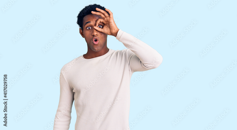 African handsome man wearing casual winter sweater doing ok gesture shocked with surprised face, eye looking through fingers. unbelieving expression. African handsome man wearing casual winter sweater doing ok gesture shocked with surprised face, eye looking through fingers. unbelieving expression.