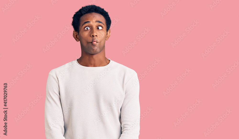 African handsome man wearing casual winter sweater making fish face with lips, crazy and comical gesture. funny expression. African handsome man wearing casual winter sweater making fish face with lips, crazy and comical gesture. funny expression.