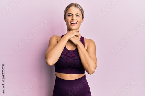 Beautiful blonde woman wearing sportswear over pink background shouting and suffocate because painful strangle. health problem. asphyxiate and suicide concept.