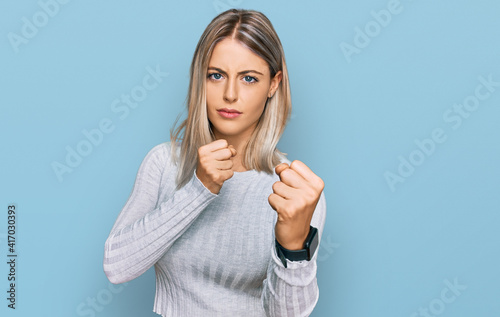 Beautiful blonde woman wearing casual clothes ready to fight with fist defense gesture, angry and upset face, afraid of problem