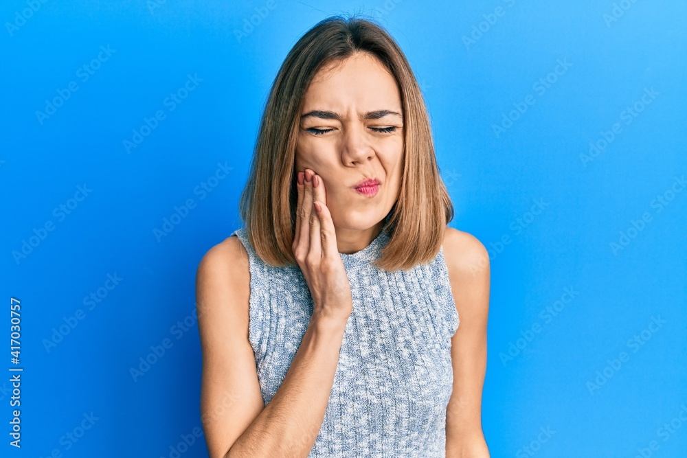 Young caucasian blonde woman wearing casual t shirt touching mouth with hand with painful expression because of toothache or dental illness on teeth. dentist Young caucasian blonde woman wearing casual t shirt touching mouth with hand with painful expression because of toothache or dental illness on teeth. dentist