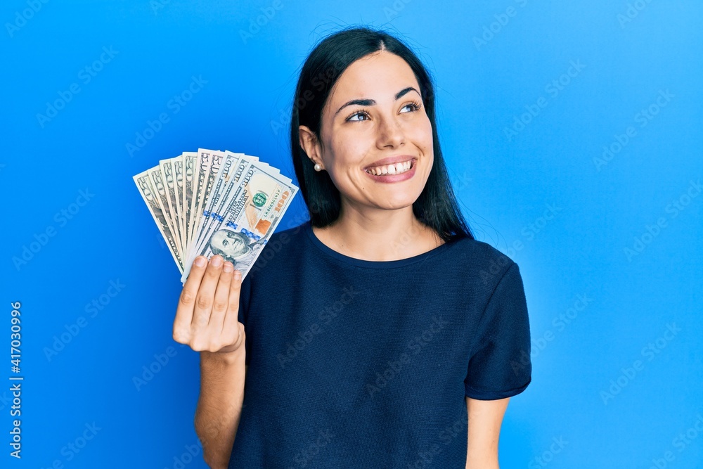Beautiful young woman holding dollars smiling looking to the side and staring away thinking. Beautiful young woman holding dollars smiling looking to the side and staring away thinking.