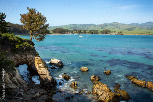 Turquoise ocean bay with white sailboat and rugged rock arch in the spring time on the beautiful central coast of California, San Simeon Cove