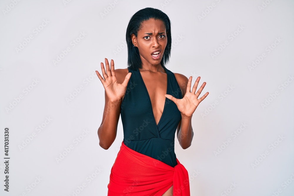 Young african american woman wearing swimsuit afraid and terrified with fear expression stop gesture with hands, shouting in shock. panic concept. Young african american woman wearing swimsuit afraid and terrified with fear expression stop gesture with hands, shouting in shock. panic concept.