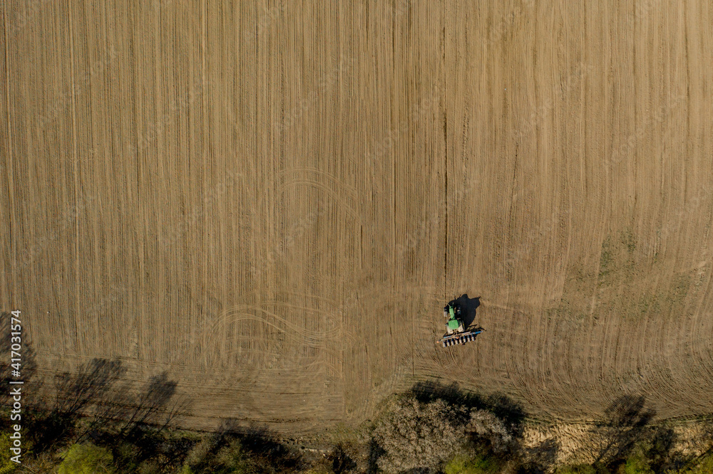 Obraz premium Aerial view large tractor cultivating a dry field. Top down aerial view tractor cultivating ground and seeding a dry field. Aerial tractor cuts furrows in farm field for sowing