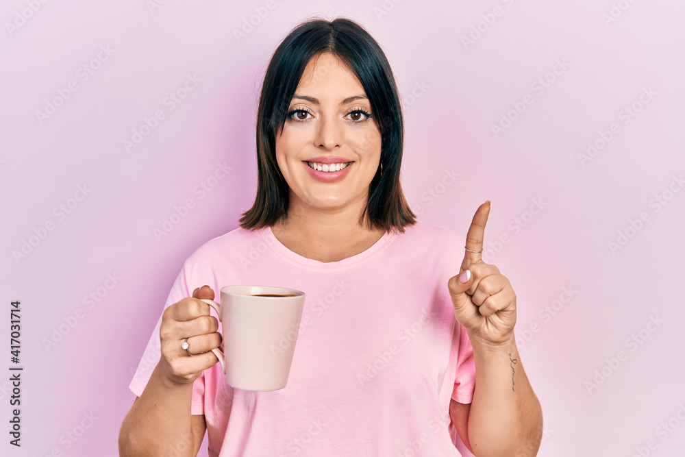 Young hispanic woman drinking a cup of coffee smiling with an idea or question pointing finger with happy face, number one Young hispanic woman drinking a cup of coffee smiling with an idea or question pointing finger with happy face, number one