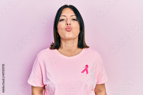 Young hispanic woman wearing pink cancer ribbon on t shirt looking at the camera blowing a kiss on air being lovely and sexy. love expression.