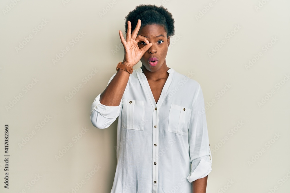 Young african american girl wearing casual clothes doing ok gesture shocked with surprised face, eye looking through fingers. unbelieving expression. Young african american girl wearing casual clothes doing ok gesture shocked with surprised face, eye looking through fingers. unbelieving expression.