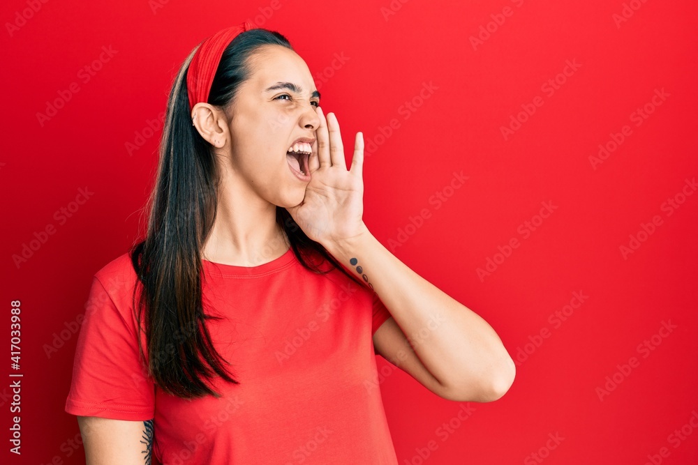 Fototapeta premium Young hispanic woman wearing casual red t shirt shouting and screaming loud to side with hand on mouth. communication concept.