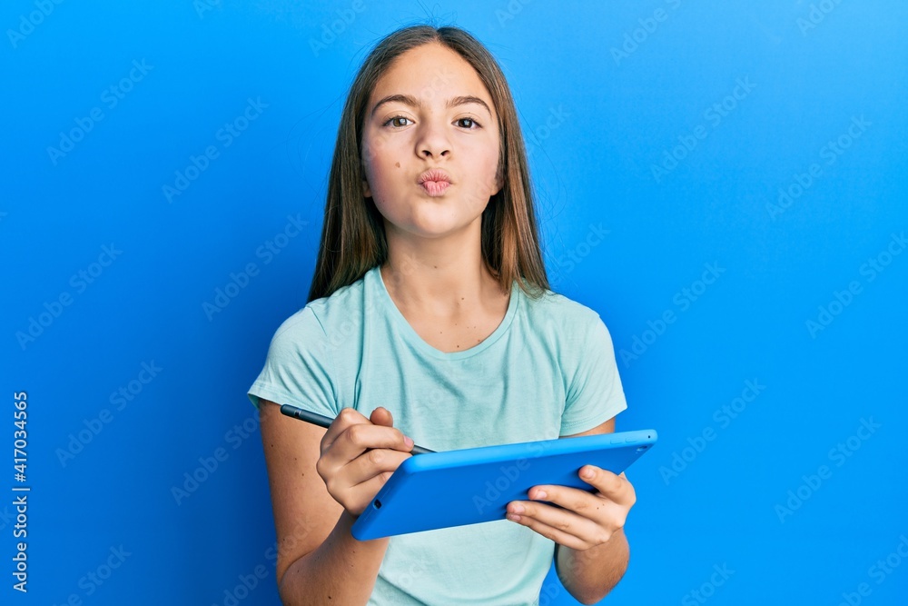 Beautiful brunette little girl using touchpad drawing on screen looking at the camera blowing a kiss being lovely and sexy. love expression. Beautiful brunette little girl using touchpad drawing on screen looking at the camera blowing a kiss being lovely and sexy. love expression.