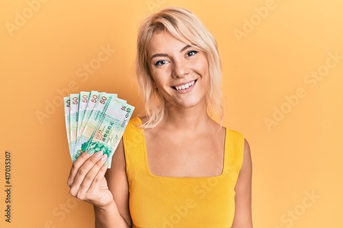 Young blonde girl holding 50 hong kong dollars banknotes looking positive and happy standing and smiling with a confident smile showing teeth