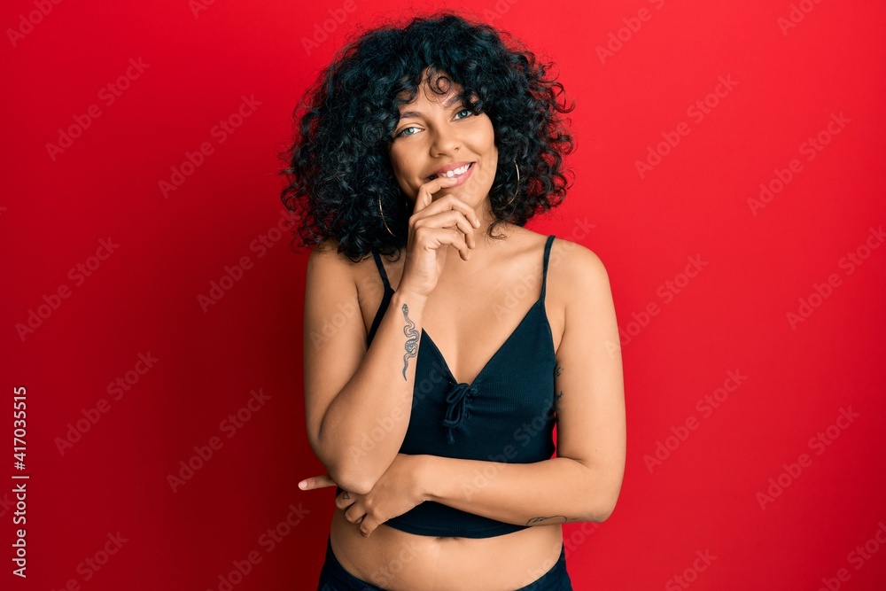 Young hispanic woman wearing casual style with sleeveless shirt looking confident at the camera with smile with crossed arms and hand raised on chin. thinking positive.