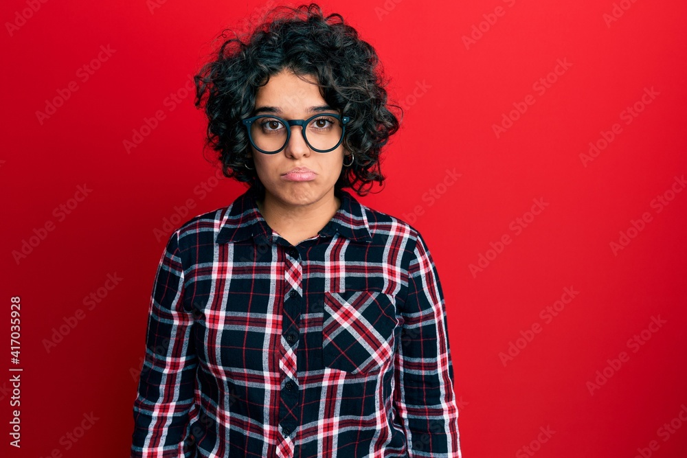 Young hispanic woman with curly hair wearing casual clothes and glasses depressed and worry for distress, crying angry and afraid. sad expression. Young hispanic woman with curly hair wearing casual clothes and glasses depressed and worry for distress, crying angry and afraid. sad expression.
