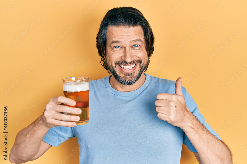 Middle age caucasian man drinking a pint of beer smiling happy and positive, thumb up doing excellent and approval sign Middle age caucasian man drinking a pint of beer smiling happy and positive, thumb up doing excellent and approval sign
